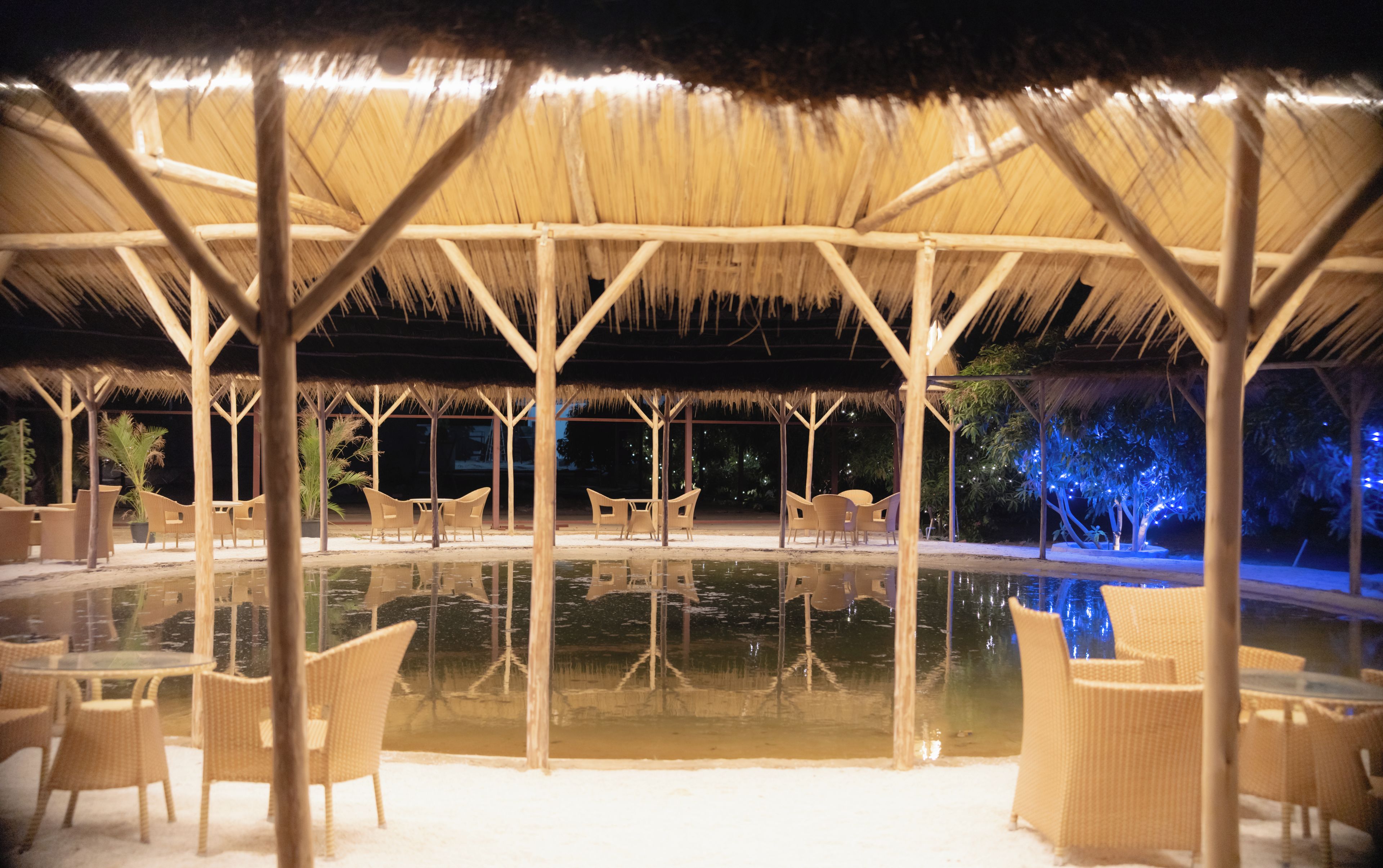 Un área de estar al aire libre con estructuras de techo de paja, rodeada por una piscina.