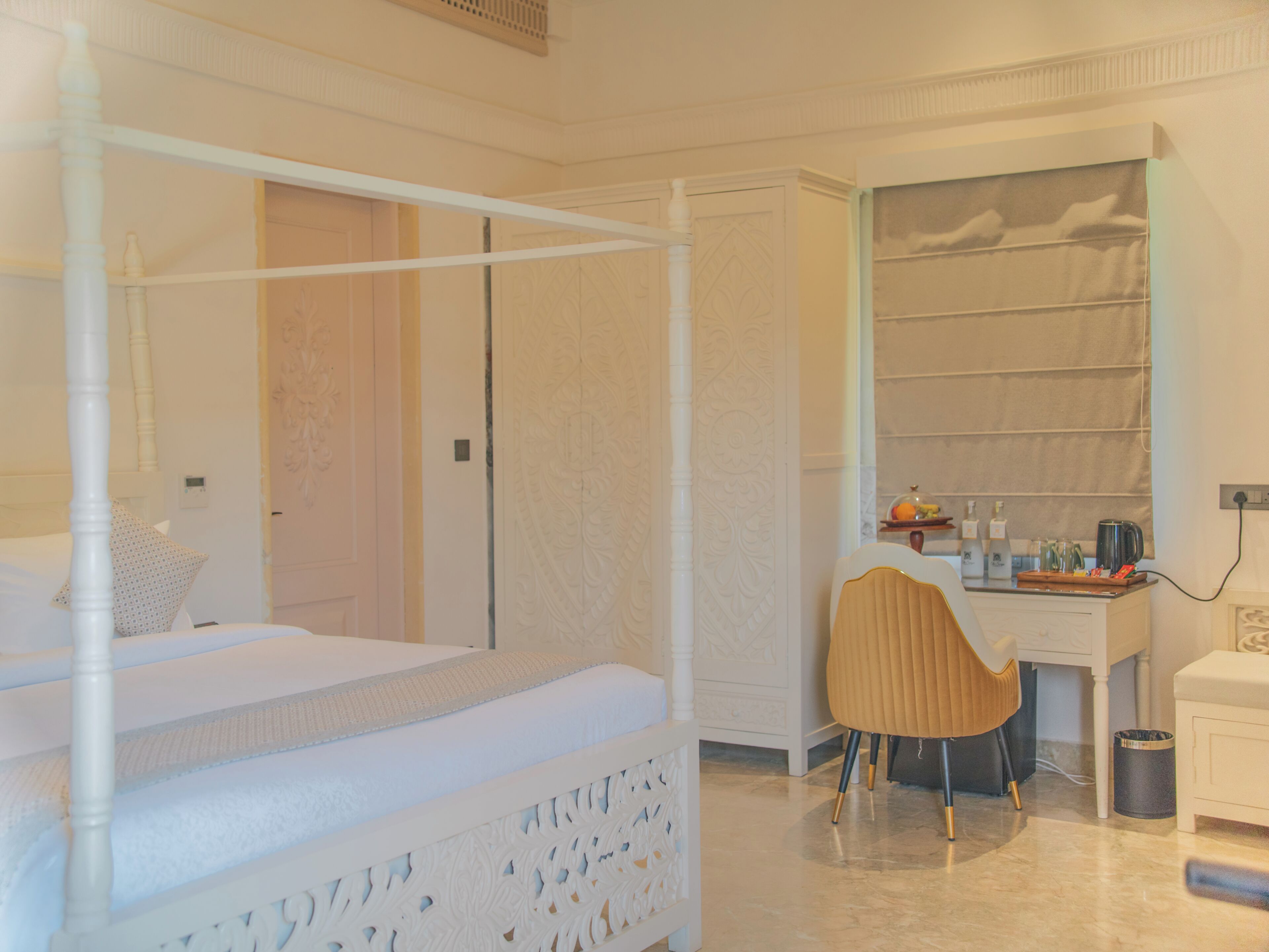 A bedroom with a four-poster bed, a desk with a chair, and a wardrobe.