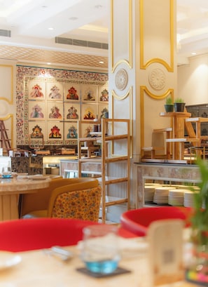 A restaurant interior with a traditional decor, featuring a central display of framed artwork, wooden furniture, and a variety of seating arrangements. - The Surya Golden Palace Pushkar (Pushkar)