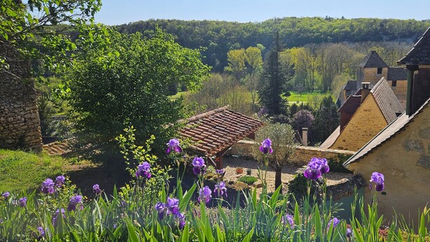 A traditional stone building with a tiled roof, surrounded by lush greenery and purple flowers. - LITTLE HAVEN OF PEACE (Les Eyzies)