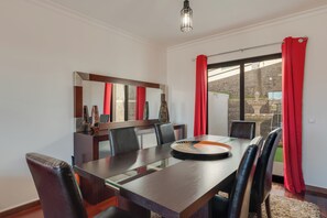 A dining area with a long table, red curtains, and a large mirror. - Andrade's Villa by HRM (Santa Cruz)