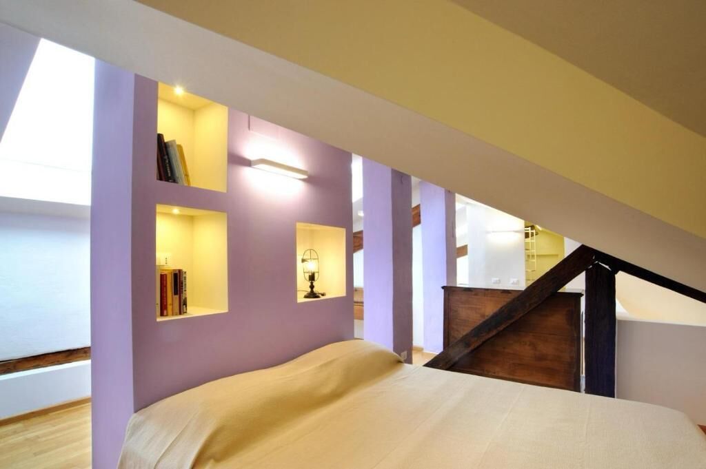 Um quarto com uma cama, estantes embutidas com livros, uma luminária e uma escada.
