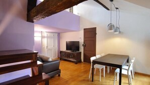 Un salon moderne avec un coin repas, des poutres en bois, un téléviseur et un escalier.
