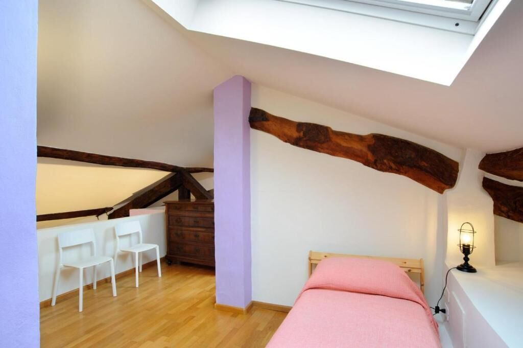 A bedroom with a skylight, a bed, a desk with chairs, and a dresser.
