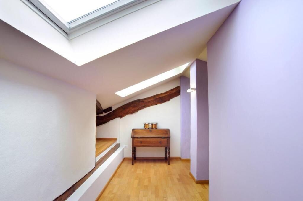Un couloir étroit avec un plafond en pente, un plancher en bois et une petite table sur laquelle reposent deux récipients.