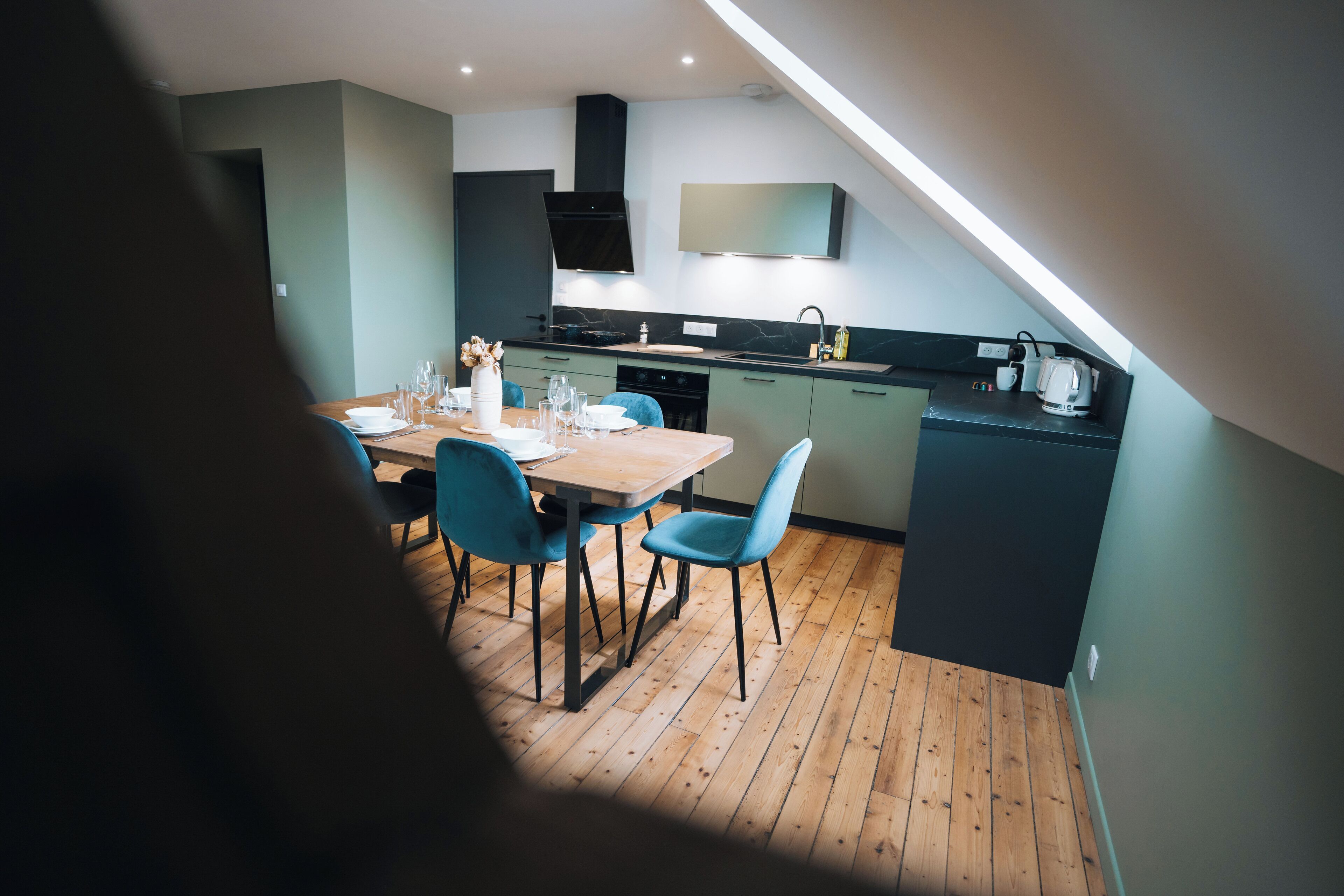 Une cuisine moderne avec un coin repas, un plancher en bois et des chaises de couleur turquoise.