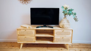 A wooden TV stand with a flat-screen TV, a vase with flowers, and a decorative mirror on the wall. - La Marjolaine - Demeure d'Hôtes (Châteauroux)