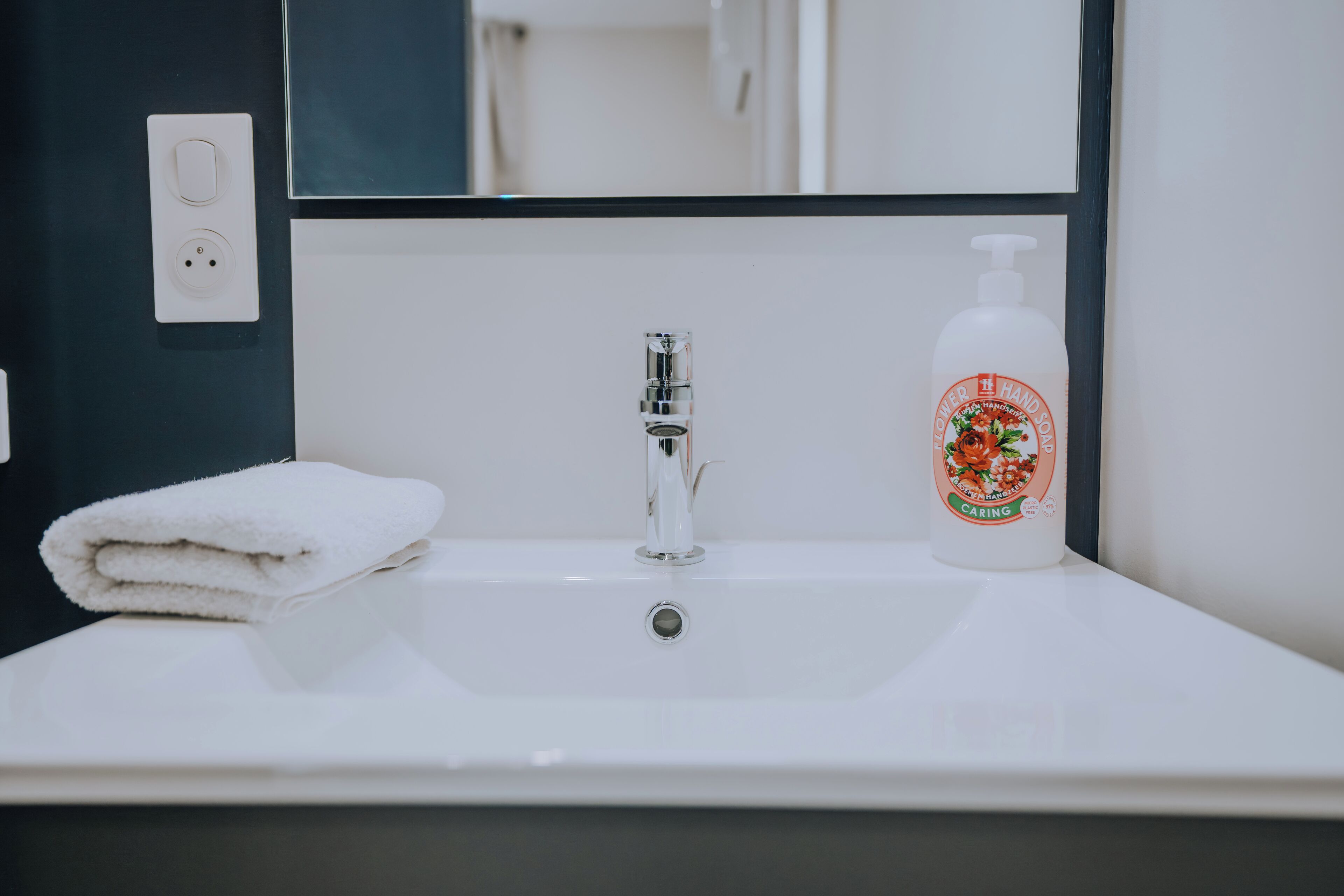 A white bathroom sink with a faucet, a white towel, and a bottle of hand soap.