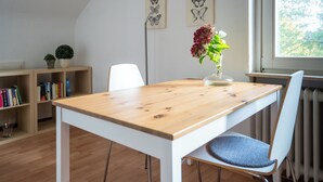 A dining area with a wooden table, white chair, bookshelves, and a window with a view. - Guesthouse Elena Apartment 21 (Kassel)