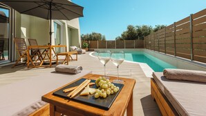 Un área junto a la piscina con una mesa de madera, dos sillas reclinables, una sombrilla grande y una piscina.