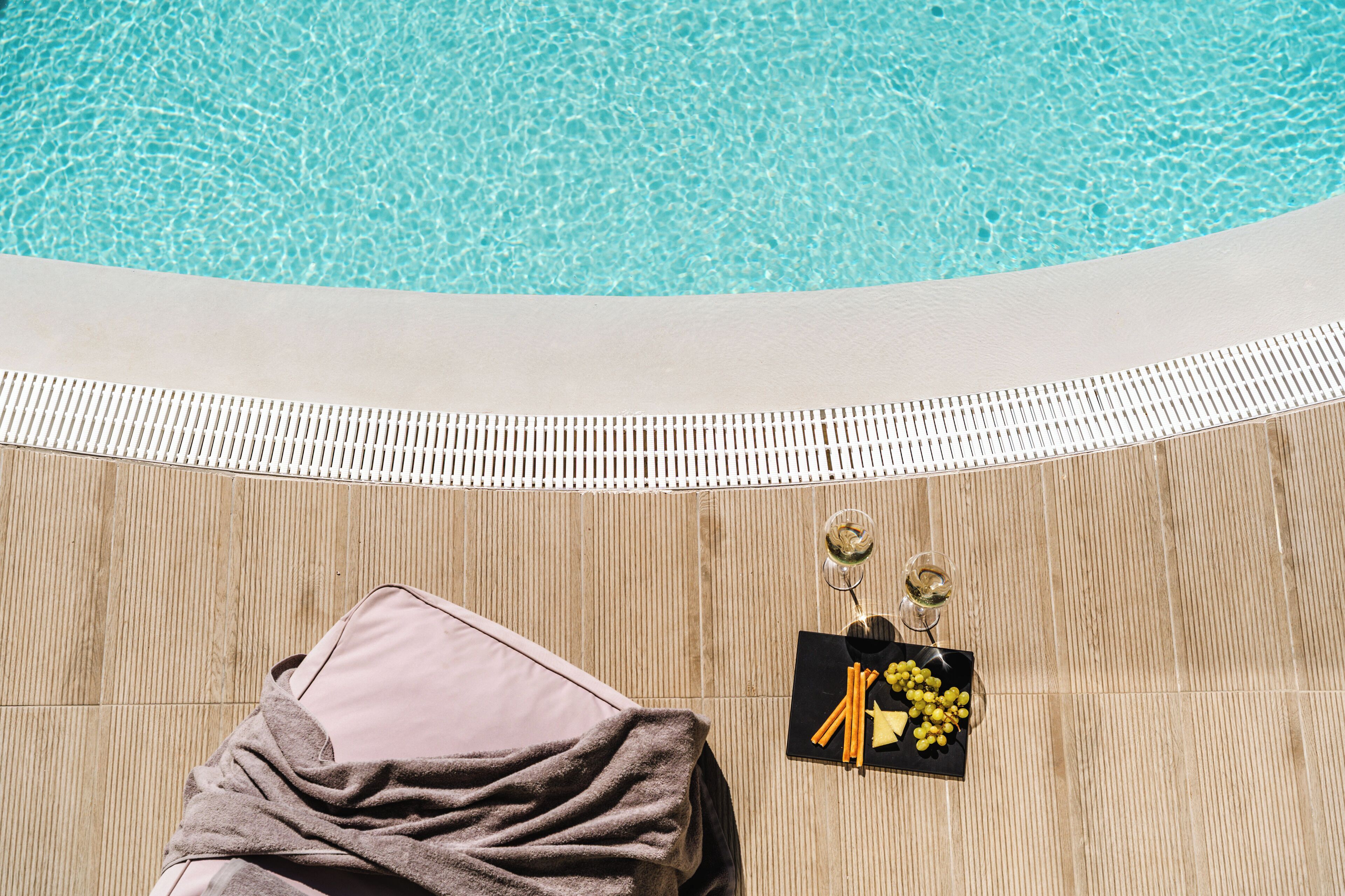 Zona de piscina con una silla de descanso, una toalla y una bandeja con comida y bebidas.