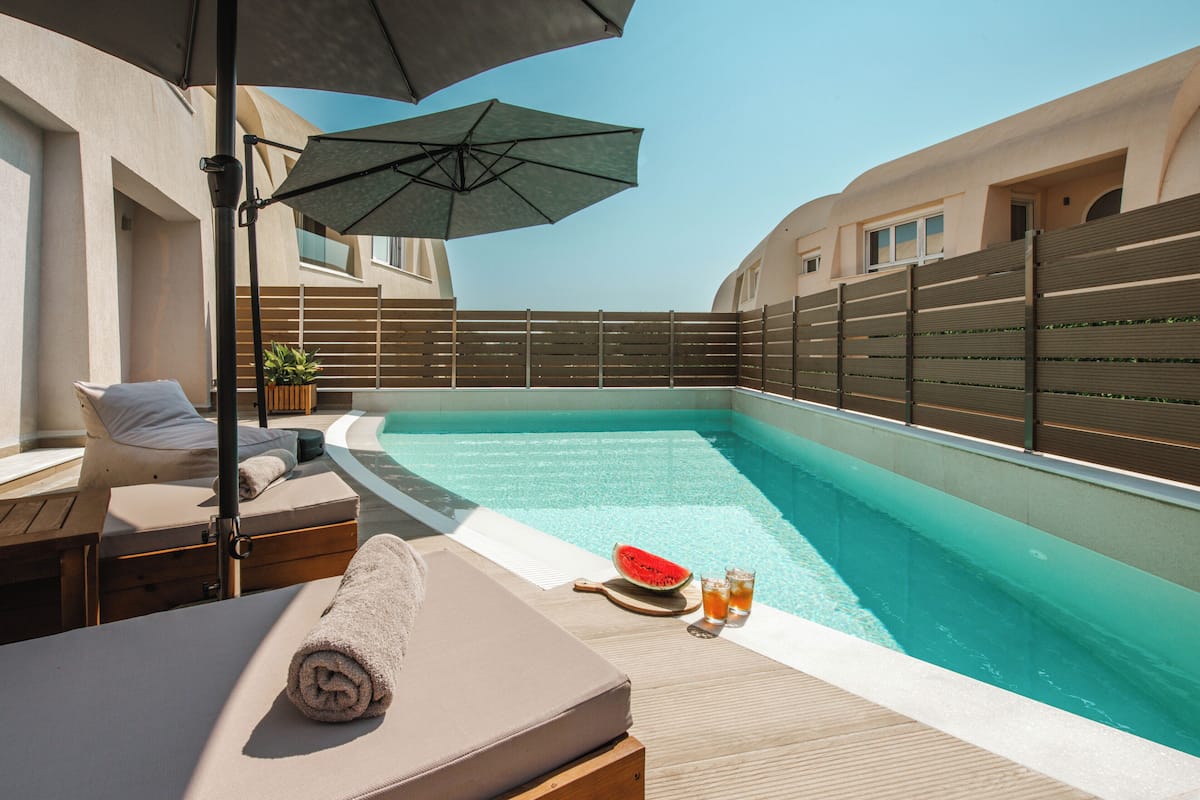 A rooftop pool area with lounge chairs, a wooden deck, and a large umbrella providing shade.