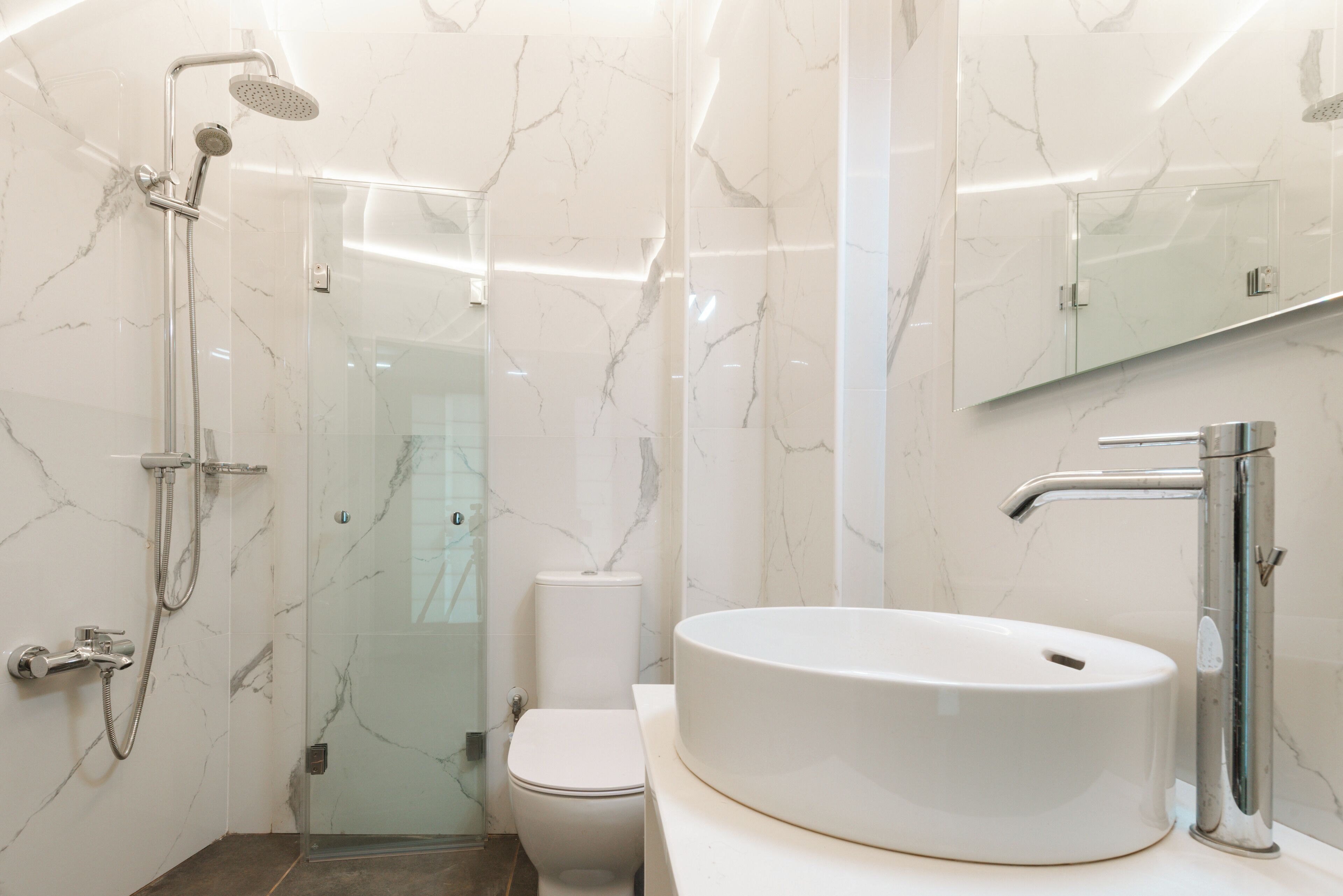 Un baño moderno con ducha de vidrio, inodoro blanco y un lavabo ovalado grande.