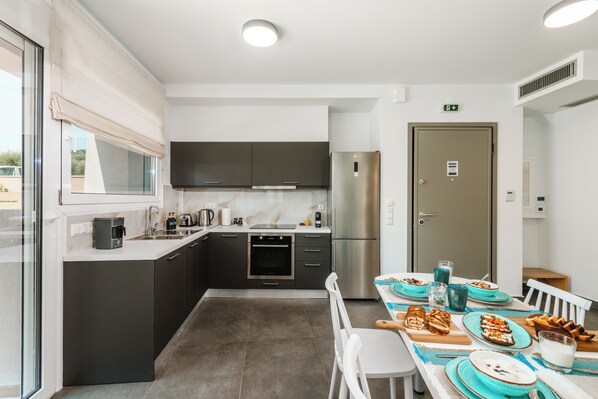 Una cocina moderna con armarios oscuros, un refrigerador de acero inoxidable y un comedor con sillas blancas y platos azules.