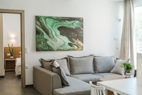 A modern living room with a grey sectional sofa, a white dining table, and a large abstract painting on the wall. - Tortuga Luxury Villas (Sivota)