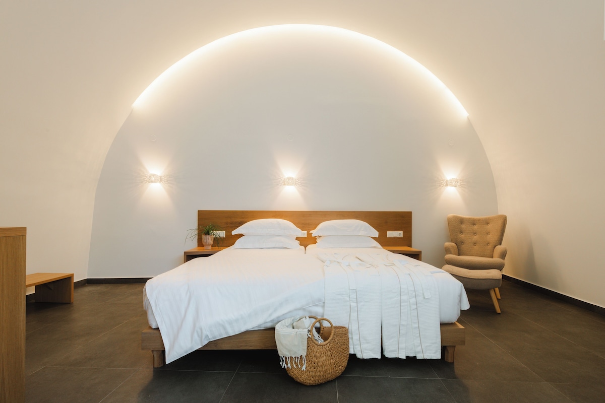 A bedroom with a curved ceiling, a bed with white bedding, a wooden nightstand, a chair, and a woven basket.