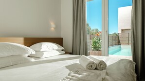 Habitación de hotel con cama, ropa de cama blanca, toalla doblada con cuidado y vistas a una piscina al aire libre.
