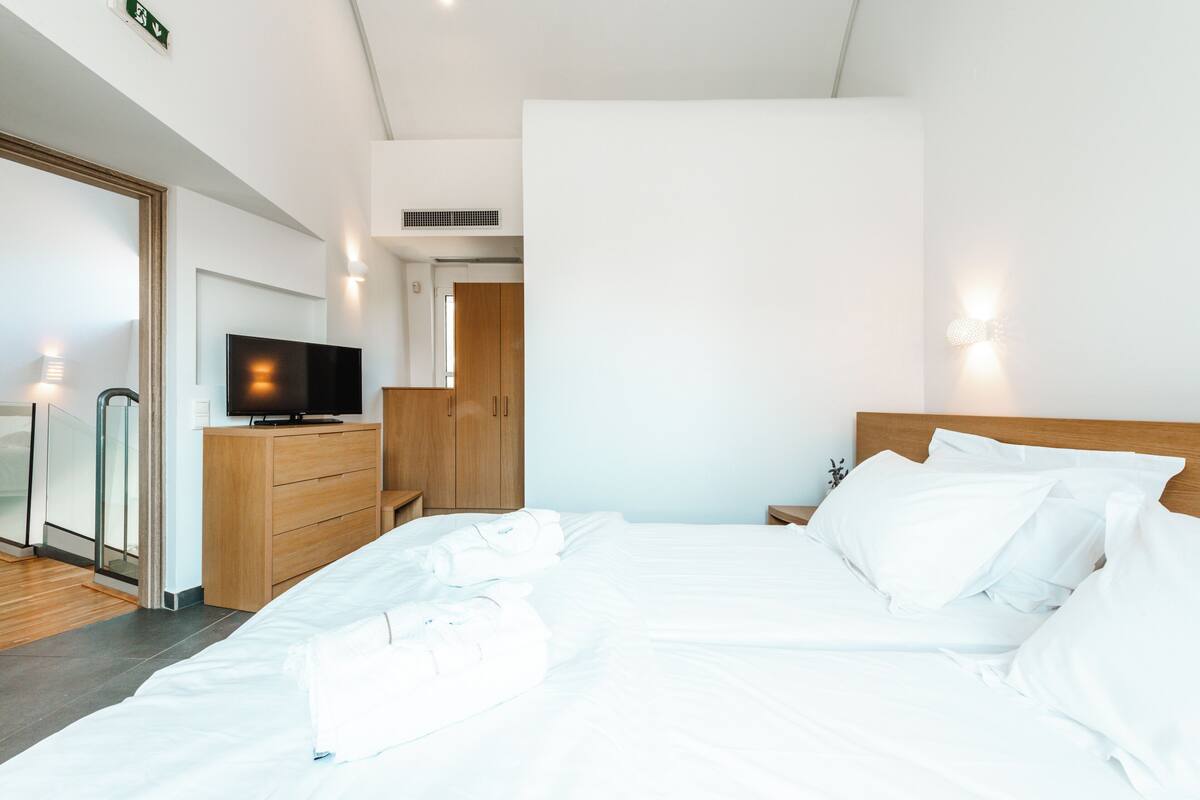 A modern hotel room with a large bed, wooden dresser, and a flat-screen TV.