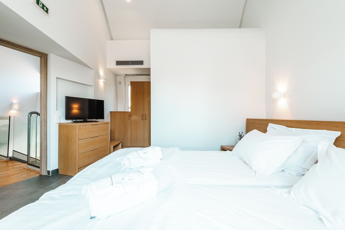 A modern hotel room with a large bed, wooden dresser, and a flat-screen TV.