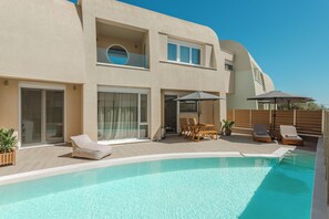 Un edificio moderno de dos pisos con piscina, mobiliario exterior y una terraza de madera.