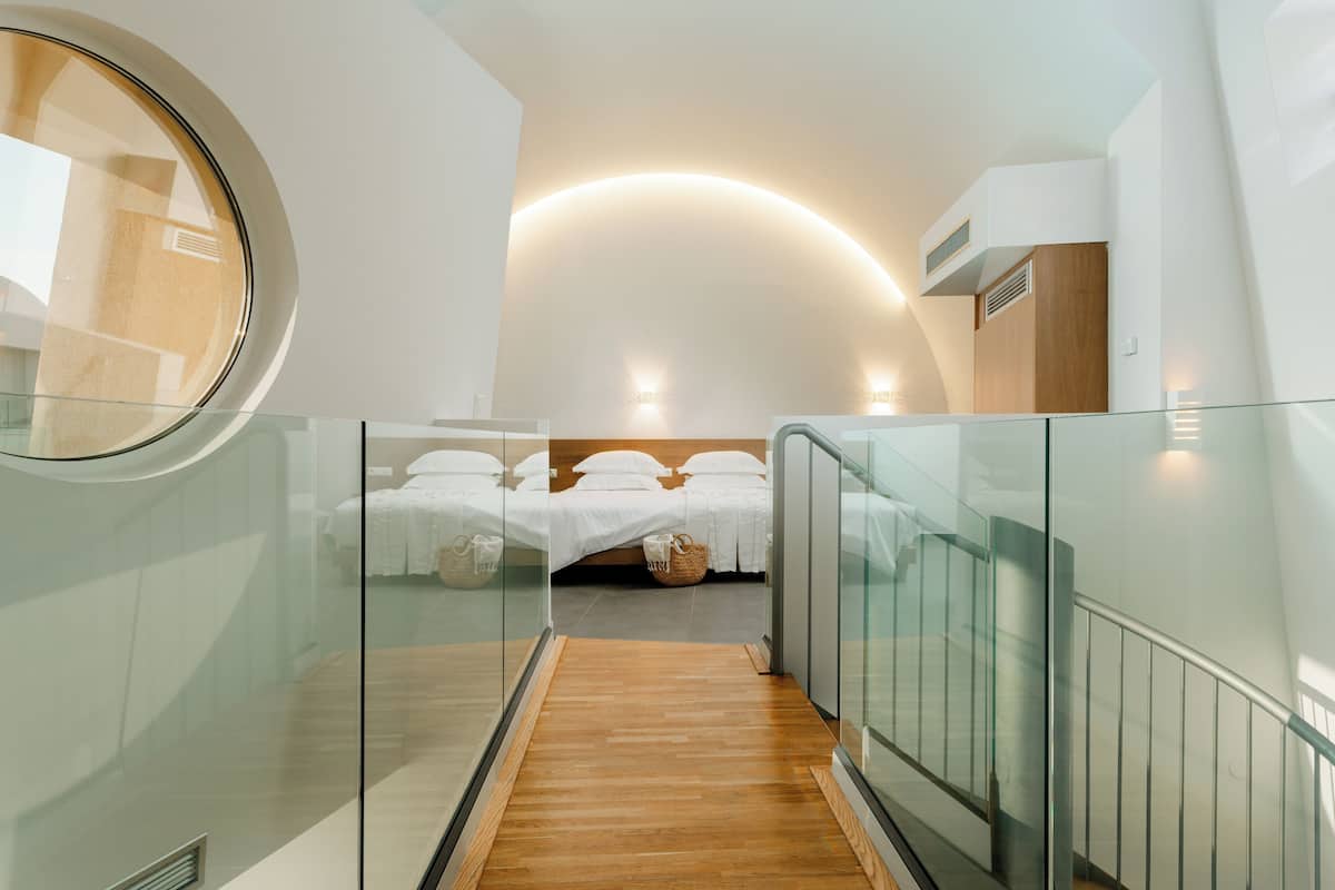 A modern hotel room with a glass-walled bed, a wooden floor, and a curved ceiling.