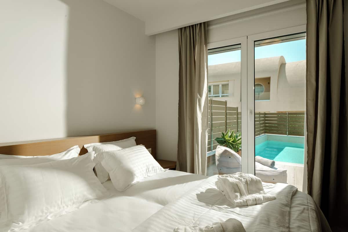 A hotel room with a large bed, a view of a swimming pool, and a balcony with a plant.
