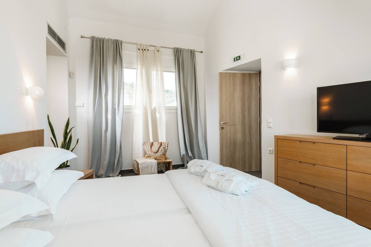 A hotel room with a large bed, a wooden dresser, a television, and a window with curtains.