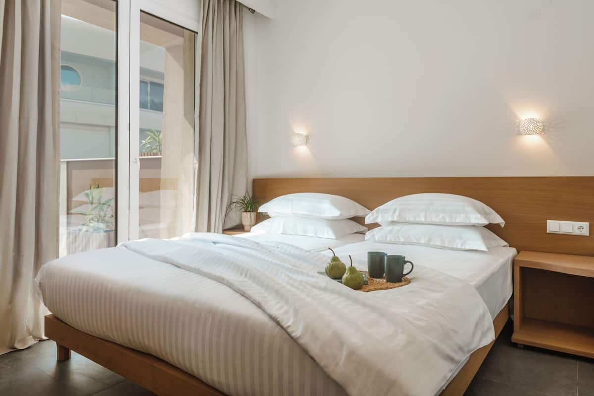 A neatly made bed with a wooden headboard, a bedside table with a plant, and a tray with pears and mugs on the bed.