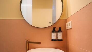 A modern bathroom with a round mirror, a white sink, and two bottles of shampoo.