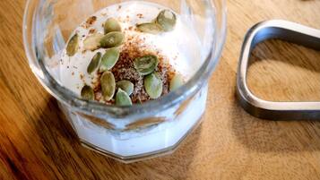 A glass bowl containing a creamy substance with pumpkin seeds and a brown spice on a wooden surface.