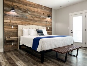 A bedroom with a wooden headboard, a bed with white bedding and a blue throw, a bedside table, and a bench. - 6 bedrooms with Private Swim Spa (Branson)