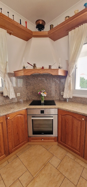 Eine Küche mit Holzausstattung, einer Granitabdeckung, einem eingebauten Backofen und einem dekorativen Regal mit verschiedenen Gegenständen.