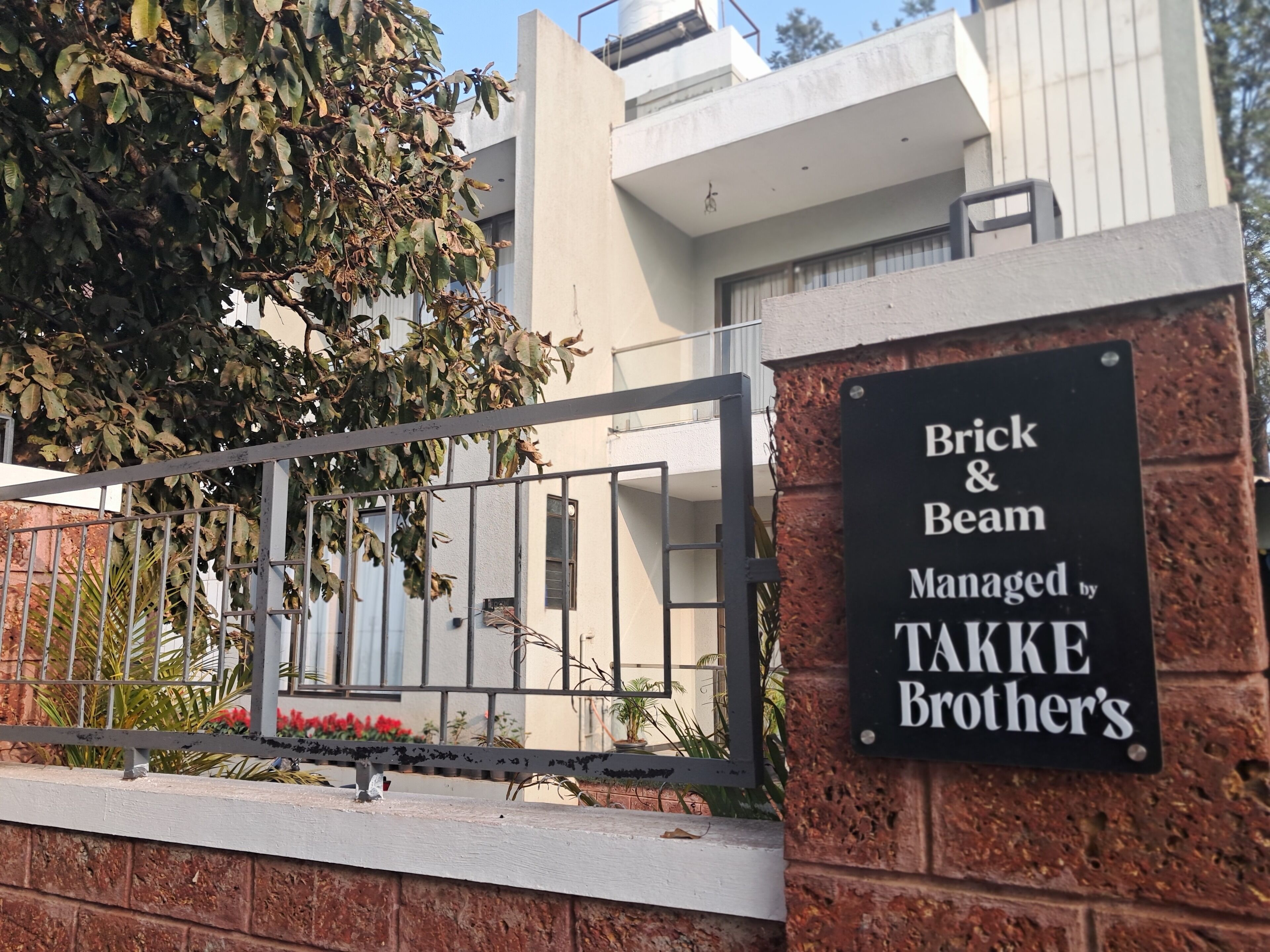 A sign for "Brick & Beam Managed by Takke Brothers" with a metal gate and a building in the background.