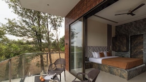 A balcony with a table, chairs, and a bed with a view of trees. - Brick and beam (Mahabaleshwar)