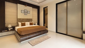 A modern bedroom with a large bed, a ceiling fan, a wall with framed pictures, and a sliding door closet. - Brick and beam (Mahabaleshwar)