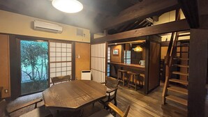 A traditional Japanese-style room with tatami flooring, a low table with chairs, a sliding door with a view of trees, and a small bar area with stools. - Family fun!　　Quiet rural space near city center by car｜Okinawa Old House Inn (石垣市)