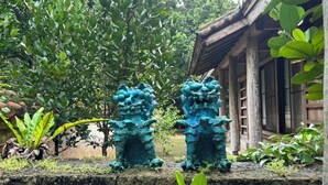 A traditional building with a tiled roof and wooden walls, surrounded by lush greenery and two stone lion statues. - Family fun!　 　Quiet rural space near city center by car｜Okinawa Old House Inn (石垣市)