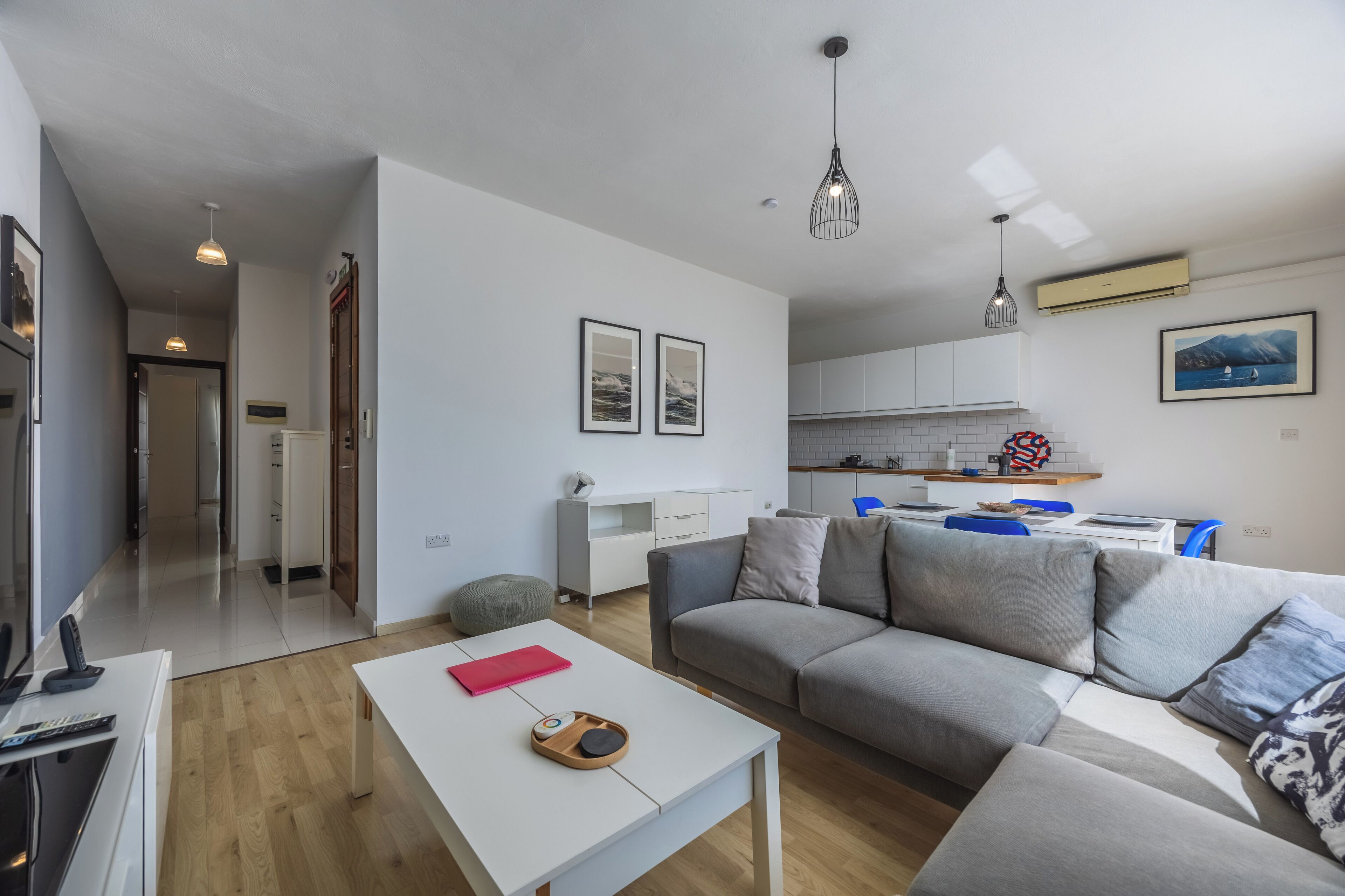 Un salon moderne avec un canapé gris, une table basse blanche et une cuisine en arrière-plan.