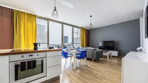 Una cocina moderna con comedor, un sofá y una televisión en una sala de estar con ventanas amplias.