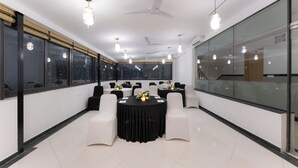 A conference room with round tables, white chairs, and pendant lighting. - Hotel Rivido Near Manyata Tech park (Bengaluru)