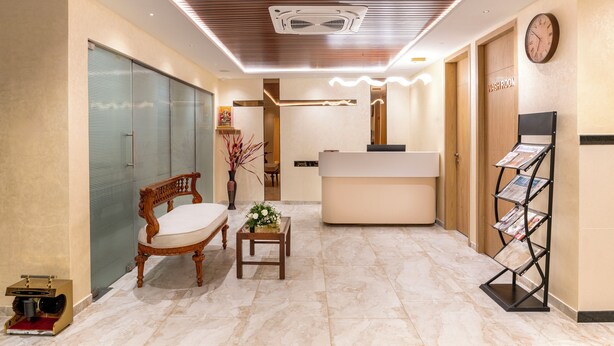 A reception area with a wooden reception desk, a clock, a magazine rack, and a bench with a vase of flowers. - Hotel Rivido Near Manyata Tech park (Bengaluru)