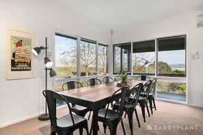 Ein Essbereich mit einem langen Tisch und Stühlen, großen Fenstern und einem gerahmten Poster an der Wand.