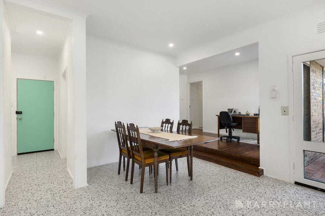 A spacious room with a dining table and chairs, a desk with a chair, and a green door.