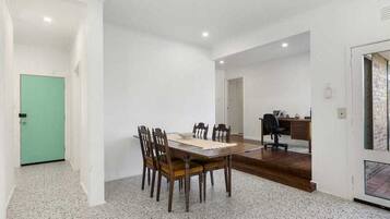 A spacious room with a dining table and chairs, a desk with a chair, and a green door.