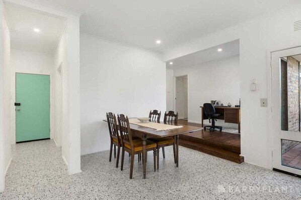 Une pièce spacieuse comprenant une table à manger et des chaises, un bureau avec une chaise, et une porte verte.