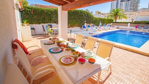 A dining area with a poolside view, featuring a table set for a meal, outdoor chairs, and a pool. - Villa Catrina - Plusholidays (Calpe)