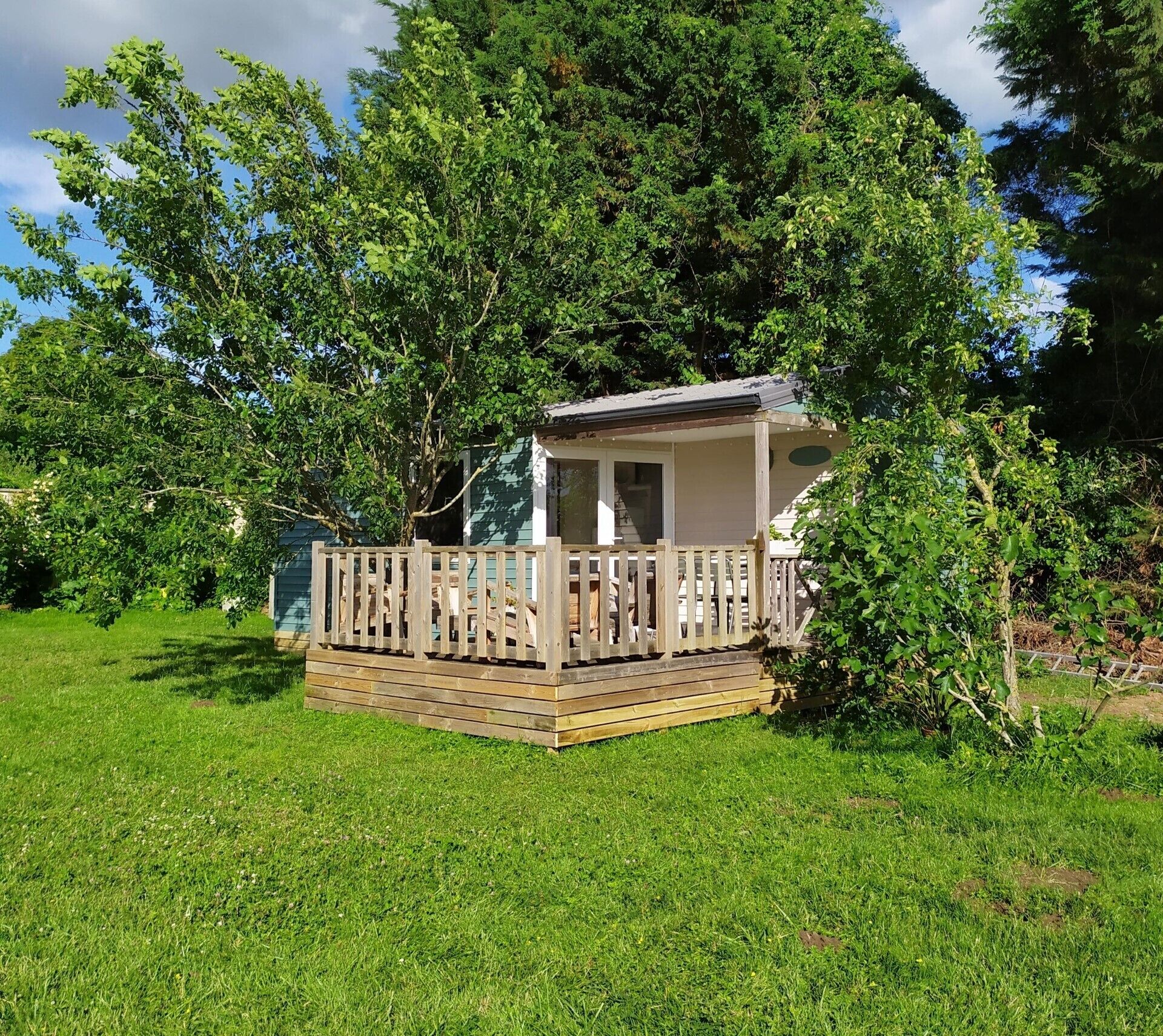 A small wooden deck with a covered seating area, surrounded by lush green grass and trees.
