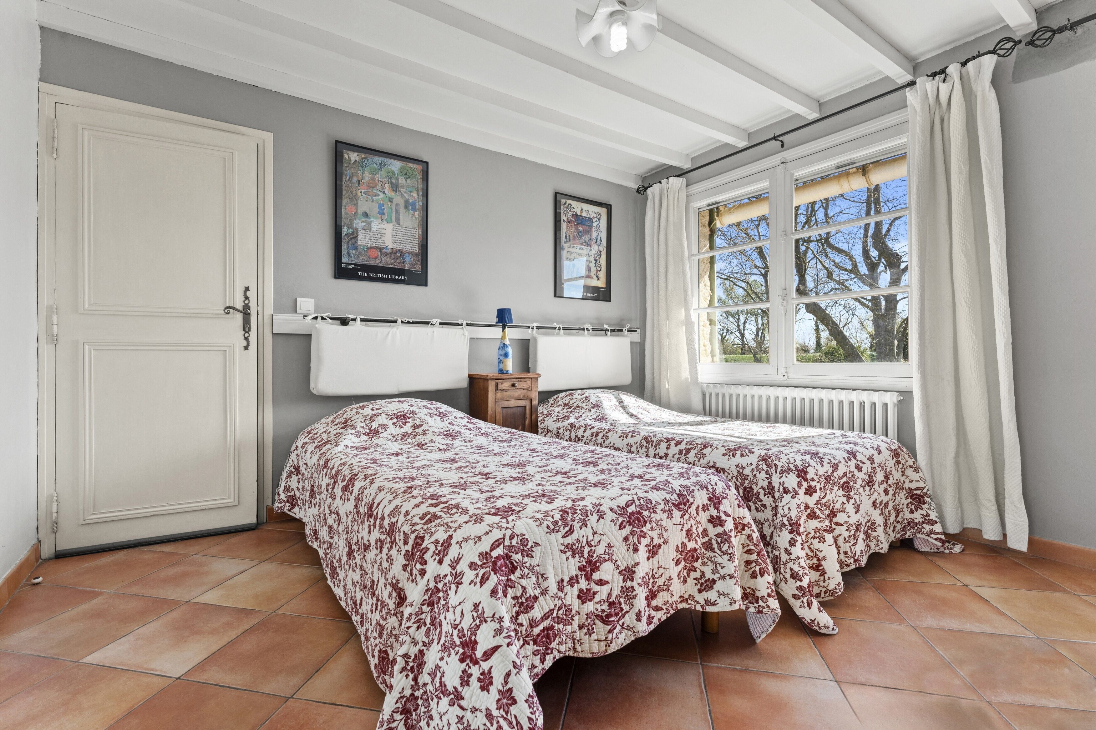 Een slaapkamer met twee bedden, een radiator, een raam met gordijnen en een deur.