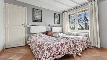 Een slaapkamer met twee bedden, een radiator, een raam met gordijnen en een deur.