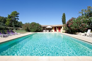 Una piscina con sillas de descanso, un edificio con techo de tejas y follaje circundante.